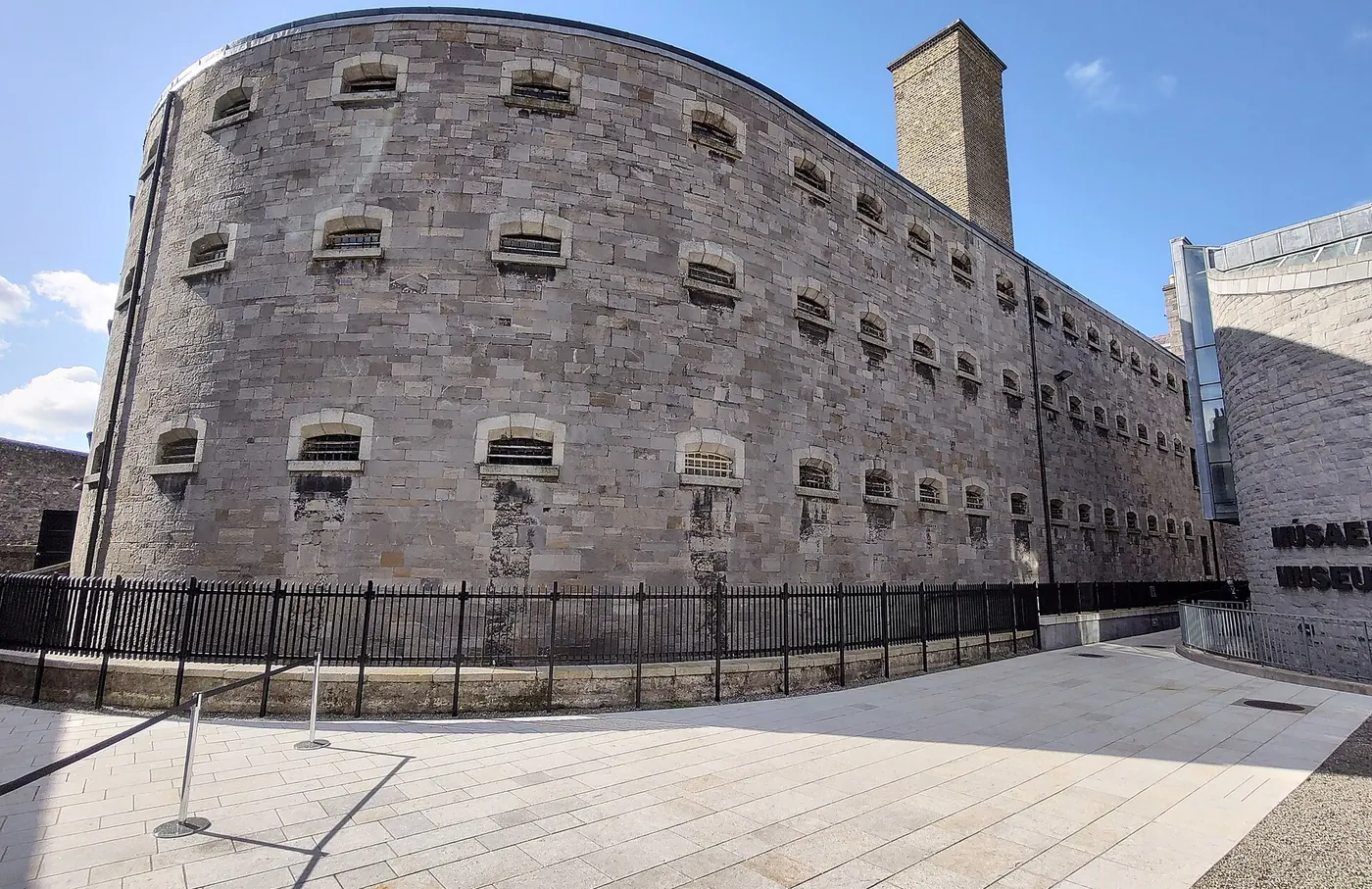 The curved stone wall of Kilmainham Gaol in Dublin under a blue sky